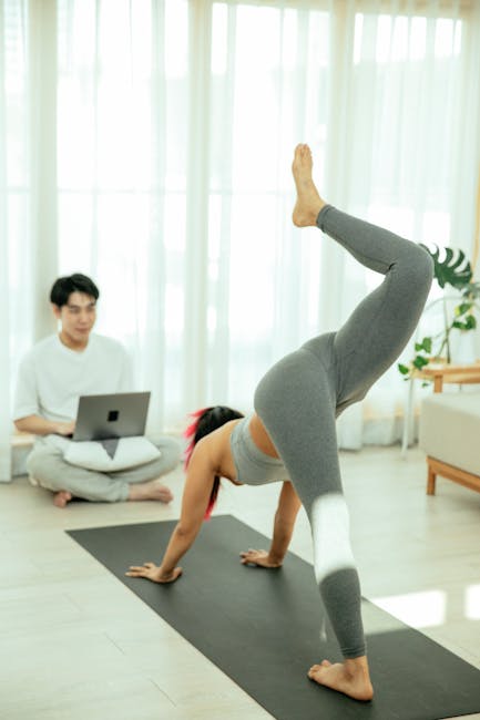 Man wearing activewear stretching on a yoga mat by a large window at home.